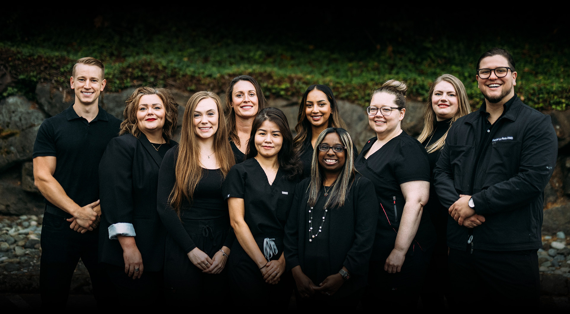 Team photo of staff at Travelle Family Dentistry office in Burien, WA standing outside in front of a garden